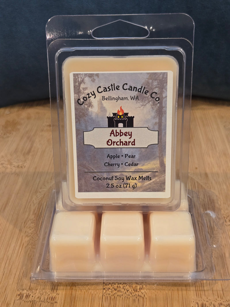 Candle wax melts in a clear packaging with a label on a wooden surface. Abbey Orchard, with notes of Apple, Pear, Cherry, and Cedar.
