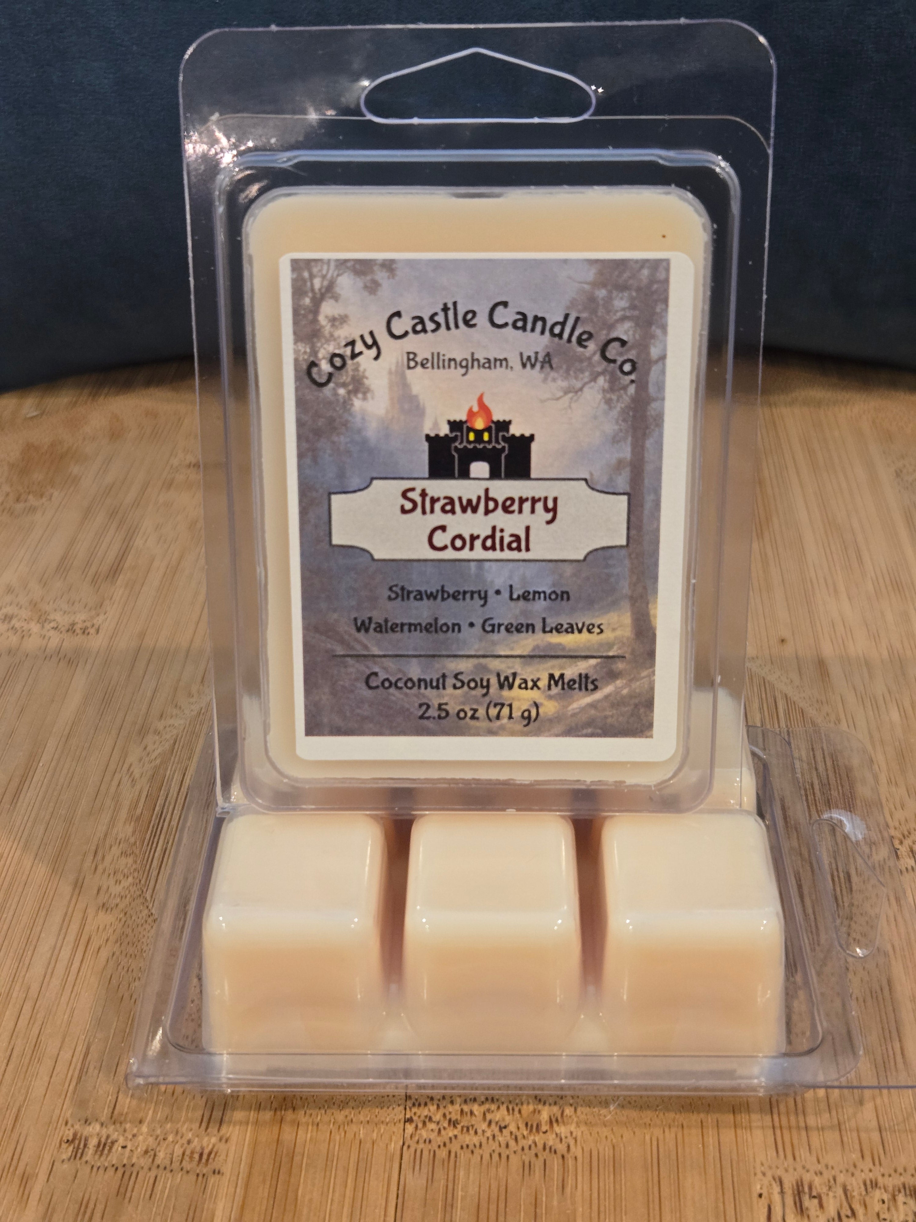 Packaged strawberry cordial wax melts on a wooden surface. Strawberry Cordial, with notes of Strawberry, Lemon, Watermelon, and Green Leaves.